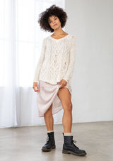 [Color: Vanilla] A front facing image of a brunette model wearing a lightweight cable knit pullover with open knit details. Featuring a classic round neckline, dropped shoulders, long sleeves, and a shirttail hem. Laid-back boho style for casual outings. 