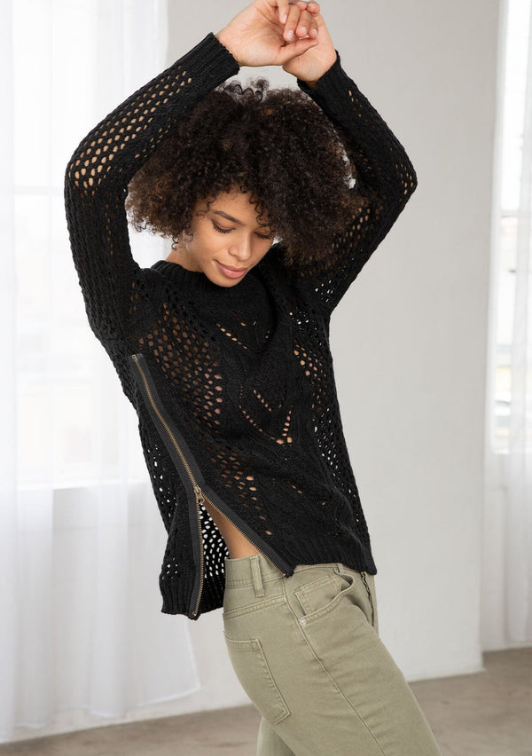 [Color: Black] An image of a brunette model wearing a black crochet pullover sweater with a side zipper accent. Featuring a crew neckline, long sleeves, and rib trim. 