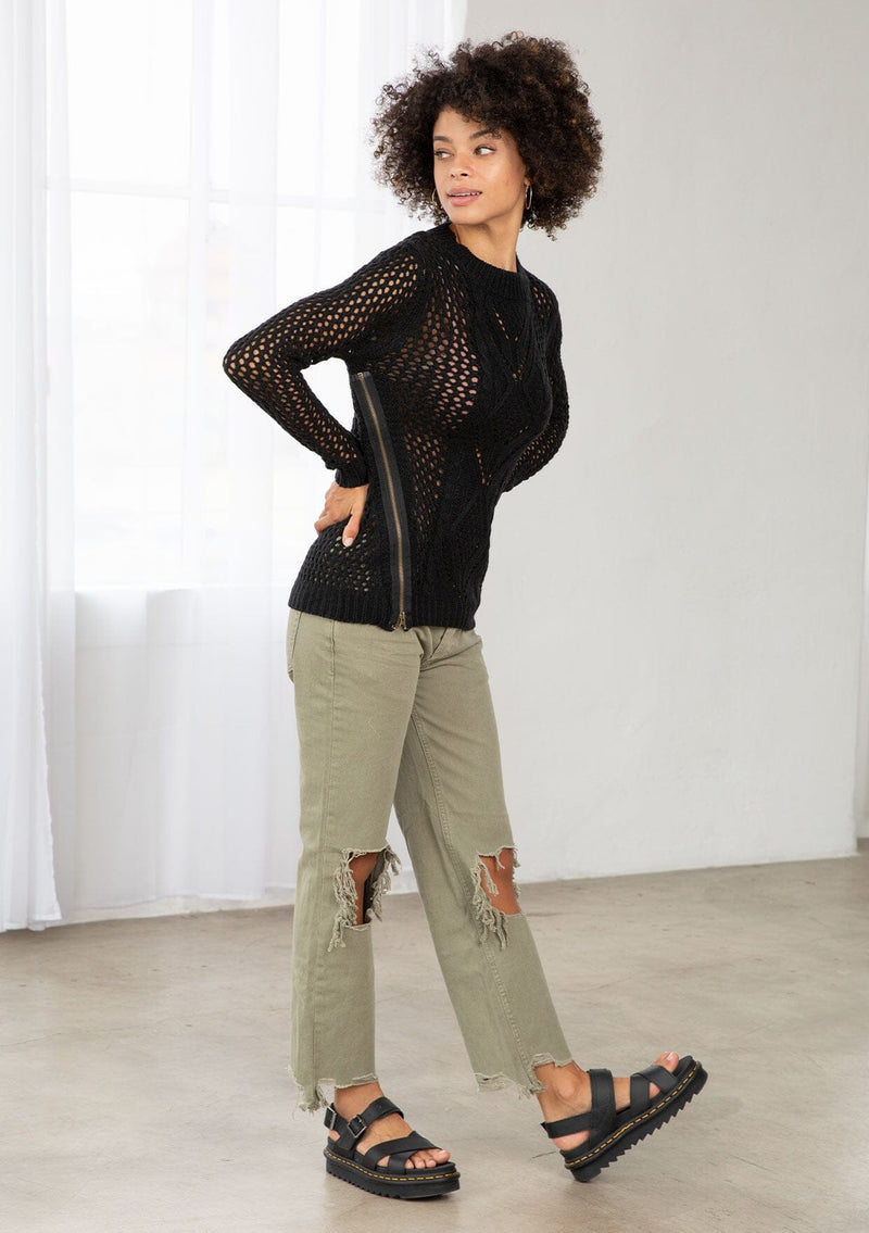 [Color: Black] An image of a brunette model wearing a black crochet pullover sweater with a side zipper accent. Featuring a crew neckline, long sleeves, and rib trim. 