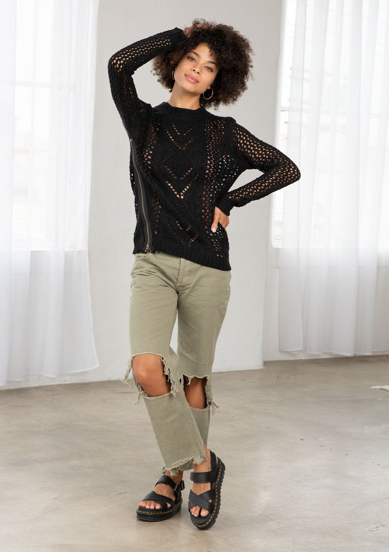 [Color: Black] An image of a brunette model wearing a black crochet pullover sweater with a side zipper accent. Featuring a crew neckline, long sleeves, and rib trim. 