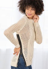[Color: Natural] An image of a brunette model wearing a beige crochet pullover sweater with a side zipper accent. Featuring a crew neckline, long sleeves, and rib trim. 