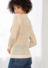 [Color: Natural] An image of a brunette model wearing a beige crochet pullover sweater with a side zipper accent. Featuring a crew neckline, long sleeves, and rib trim. 