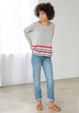 [Color: Silver/Multi] A front facing image of a brunette model wearing a grey pullover with a vibrant stripe accent. Featuring a relaxed fit, long dolman sleeves with tapered  finish, and a flattering round neckline. 