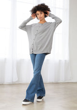 [Color: Heather Grey] A front facing image of a brunette model wearing a grey pullover button front cardigan with an asymmetrical design and long relaxed cozy sleeves. 