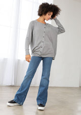 [Color: Heather Grey] A front facing image of a brunette model wearing a grey pullover button front cardigan with an asymmetrical design and long relaxed cozy sleeves. 