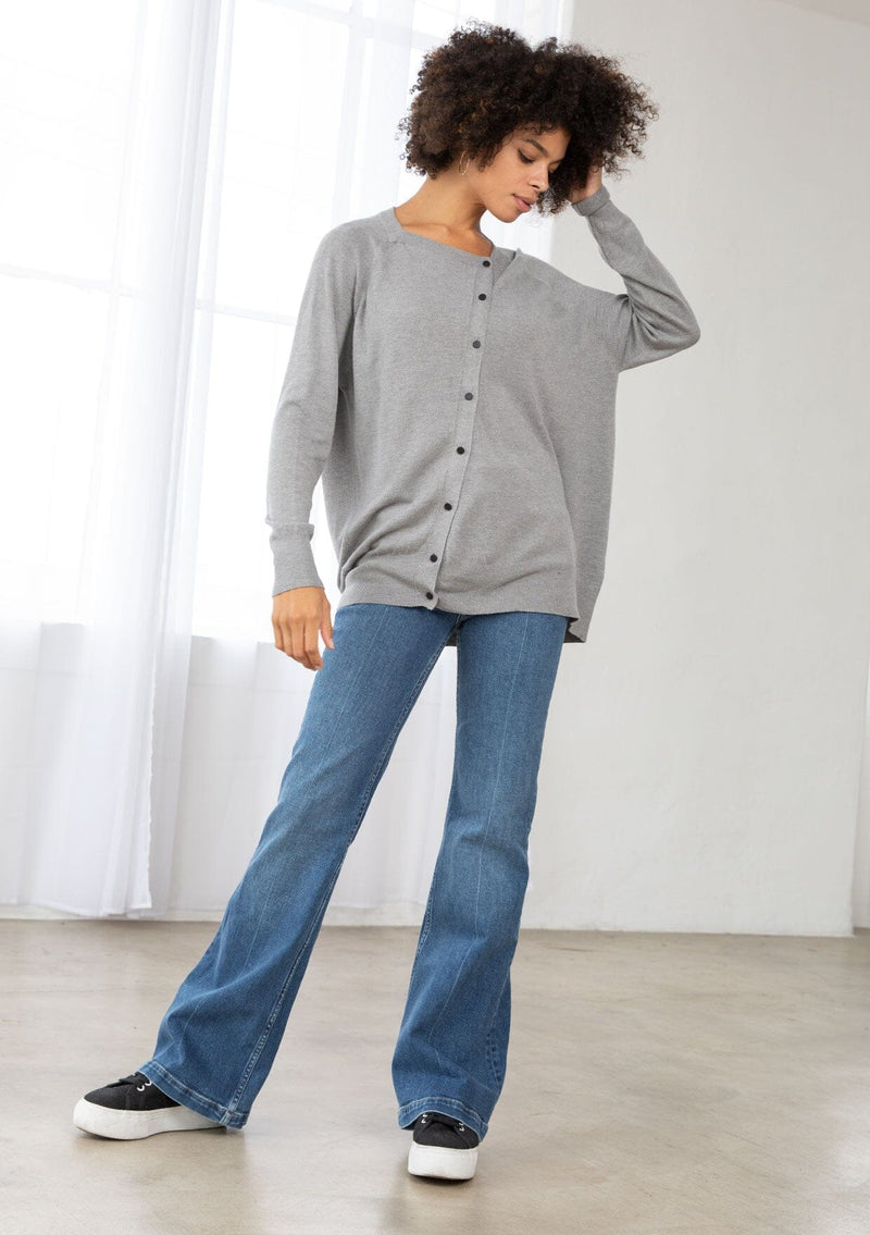 [Color: Heather Grey] A front facing image of a brunette model wearing a grey pullover button front cardigan with an asymmetrical design and long relaxed cozy sleeves. 