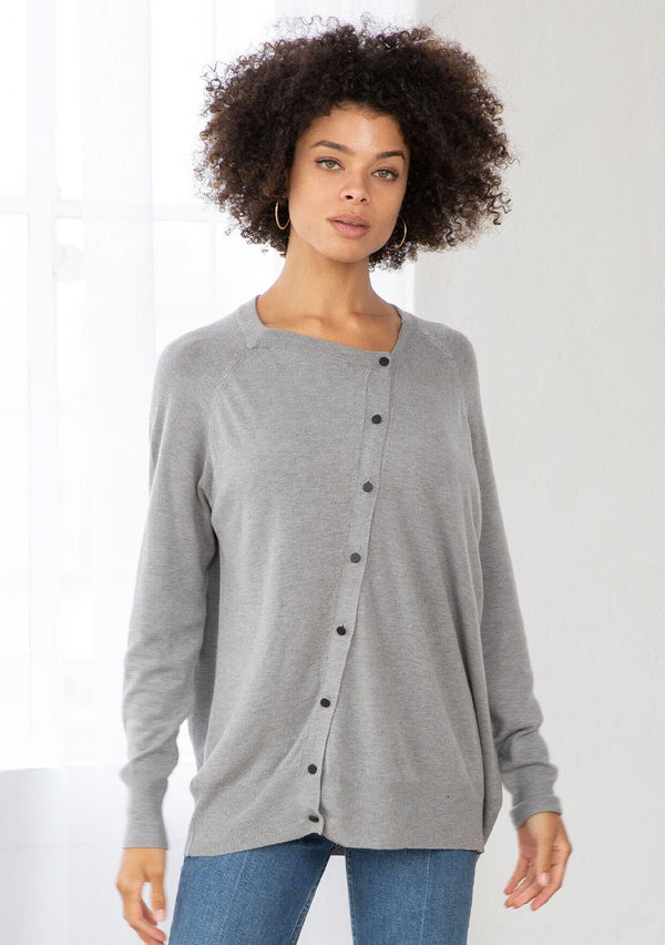 [Color: Heather Grey] A front facing image of a brunette model wearing a grey pullover button front cardigan with an asymmetrical design and long relaxed cozy sleeves. 