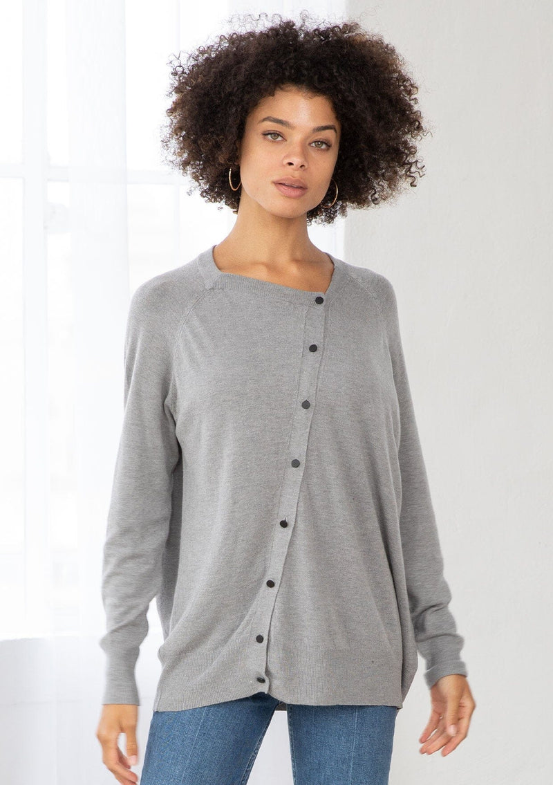 [Color: Heather Grey] A front facing image of a brunette model wearing a grey pullover button front cardigan with an asymmetrical design and long relaxed cozy sleeves. 
