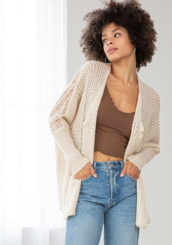 [Color: Oatmeal] A front facing image of a brunette model wearing a knit and lace beige cardigan with a hook and eye closure, batwing sleeves, and slim sleeve finish. A cozy and effortless cardigan for the fall season. 