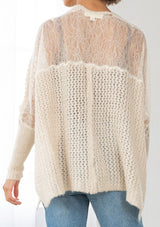 [Color: Oatmeal] A back facing image of a brunette model wearing a knit and lace beige cardigan with a hook and eye closure, batwing sleeves, and slim sleeve finish. A cozy and effortless cardigan for the fall season. 