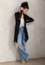 [Color: Black] A front facing image of a brunette model wearing a crochet diamond pattern cardigan with a drawstring hoodie, fringe hemline, and an open front. A classic boho layer for any season. 