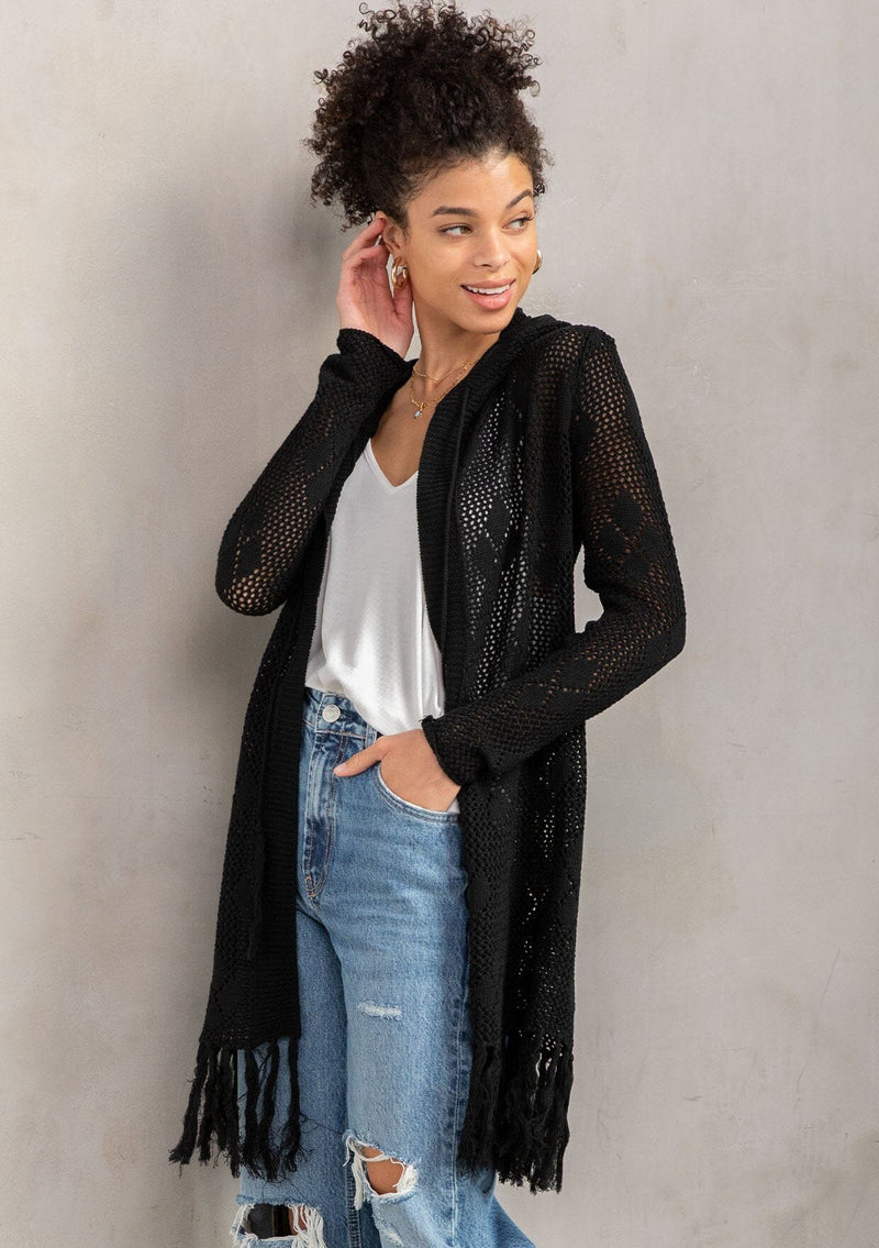 [Color: Black] A front facing image of a brunette model wearing a crochet diamond pattern cardigan with a drawstring hoodie, fringe hemline, and an open front. A classic boho layer for any season. 