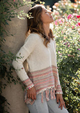 [Color: Off White/Lt Taupe] A blonde model wearing a bohemian fringed beach sweater with long sleeves and a hoodie.