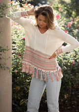 [Color: Off White/Lt Taupe] A blonde model wearing a bohemian fringed beach sweater with long sleeves and a hoodie.