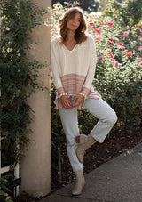 [Color: Off White/Lt Taupe] A blonde model wearing a bohemian fringed beach sweater with long sleeves and a hoodie.