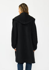 [Color: Black] A back facing image of a brunette model wearing a best selling black oversized cardigan. A cozy and thick sweater coat with a hood, an open front, side pockets, a cocoon style silhouette, and a mid length hem. 