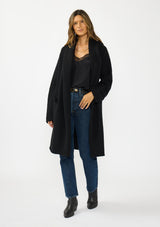 [Color: Black] A front facing image of a brunette model wearing a best selling black oversized cardigan. A cozy and thick sweater coat with a hood, an open front, side pockets, a cocoon style silhouette, and a mid length hem. 
