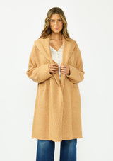 [Color: Camel] A front facing image of a brunette model wearing a best selling oversized cardigan in a camel brown color. A cozy and thick sweater coat with a hood, an open front, side pockets, a cocoon style silhouette, and a mid length hem. 