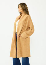 [Color: Camel] A side facing image of a brunette model wearing a best selling oversized cardigan in a camel brown color. A cozy and thick sweater coat with a hood, an open front, side pockets, a cocoon style silhouette, and a mid length hem. 