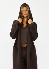 [Color: Chocolate] A half body image of a brunette model wearing a best selling brown oversized cardigan. A cozy and thick sweater coat with a hood, an open front, side pockets, a cocoon style silhouette, and a mid length hem. 