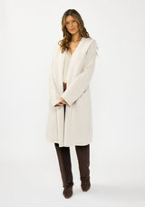 [Color: Oyster] A front facing image of a brunette model wearing a best selling off white oversized cardigan. A cozy and thick sweater coat with a hood, an open front, side pockets, a cocoon style silhouette, and a mid length hem. 