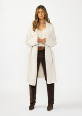 [Color: Oyster] A front facing image of a brunette model wearing a best selling off white oversized cardigan. A cozy and thick sweater coat with a hood, an open front, side pockets, a cocoon style silhouette, and a mid length hem. 