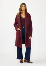 [Color: Wine] A front facing image of a brunette model wearing a best selling burgundy oversized cardigan. A cozy and thick sweater coat with a hood, an open front, side pockets, a cocoon style silhouette, and a mid length hem. 