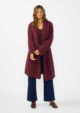 [Color: Wine] A front facing image of a brunette model wearing a best selling burgundy oversized cardigan. A cozy and thick sweater coat with a hood, an open front, side pockets, a cocoon style silhouette, and a mid length hem. 