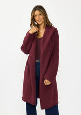 [Color: Wine] A front facing image of a brunette model wearing a best selling burgundy oversized cardigan. A cozy and thick sweater coat with a hood, an open front, side pockets, a cocoon style silhouette, and a mid length hem. 