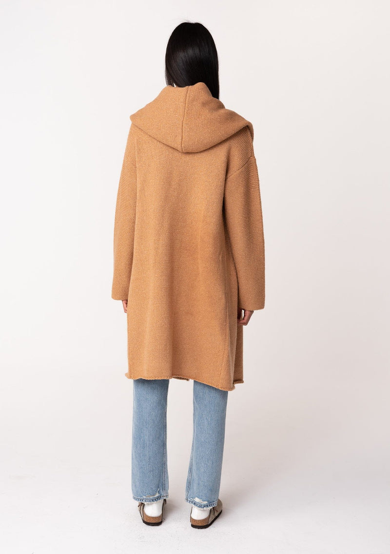 [Color: Camel] A back facing image of a brunette model wearing a best selling oversized cardigan in a camel brown color. A cozy and thick sweater coat with a hood, an open front, side pockets, a cocoon style silhouette, and a mid length hem. 
