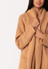 [Color: Camel] A close up front facing image of a brunette model wearing a best selling oversized cardigan in a camel brown color. A cozy and thick sweater coat with a hood, an open front, side pockets, a cocoon style silhouette, and a mid length hem. 