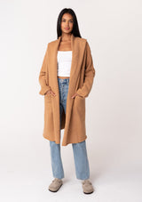 [Color: Camel] A front facing image of a brunette model wearing a best selling oversized cardigan in a camel brown color. A cozy and thick sweater coat with a hood, an open front, side pockets, a cocoon style silhouette, and a mid length hem. 