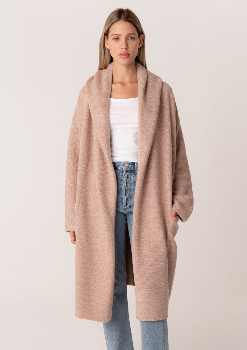 [Color: Heather Rose] A front facing image of a blonde model wearing a best selling oversized cardigan in a light pink color. A cozy and thick sweater coat with a hood, an open front, side pockets, a cocoon style silhouette, and a mid length hem. 