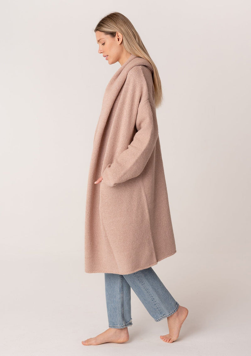 [Color: Heather Rose] A side facing image of a blonde model wearing a best selling oversized cardigan in a light pink color. A cozy and thick sweater coat with a hood, an open front, side pockets, a cocoon style silhouette, and a mid length hem. 