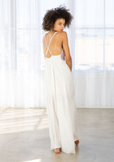 [Color: Off White/Blue/Red] A back facing image of a brunette model wearing a white sleeveless maxi dress with a blue and red embroidered bodice, a scoop neckline, and a cross back detail.