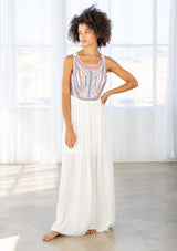 [Color: Off White/Blue/Red] A front facing image of a brunette model wearing a white sleeveless maxi dress with a blue and red embroidered bodice, a scoop neckline, and a cross back detail.