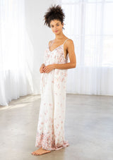 [Color: Blue Rose/Vanilla] A side facing image of a brunette model wearing a bohemian white and pink butterfly print maxi dress with a v neckline and adjustable spaghetti straps. 