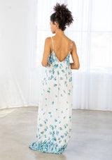 [Color: Hazel Teal/Vanilla] A back facing image of a brunette model wearing a bohemian white and blue butterfly print maxi dress with a v neckline and adjustable spaghetti straps. 
