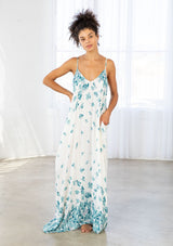 [Color: Hazel Teal/Vanilla] A front facing image of a brunette model wearing a bohemian white and blue butterfly print maxi dress with a v neckline and adjustable spaghetti straps. 