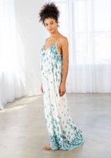 [Color: Hazel Teal/Vanilla] A side facing image of a brunette model wearing a bohemian white and blue butterfly print maxi dress with a v neckline and adjustable spaghetti straps. 
