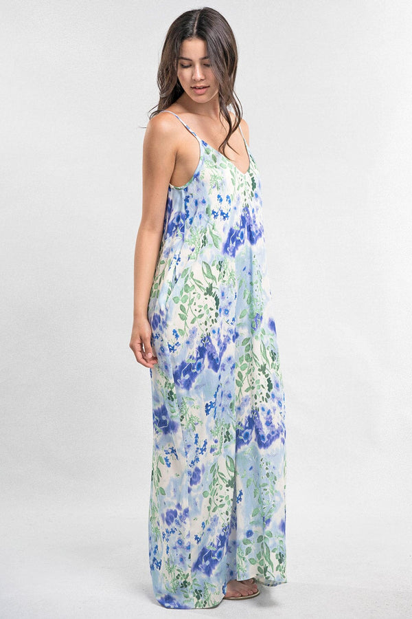 [Color: Violet/Green/Blue] A side facing image of a brunette model wearing a blue and green floral maxi dress with adjustable spaghetti straps, a v-neckline, and side pockets. A cocoon fit maxi dress for the beach and resort getaways. 