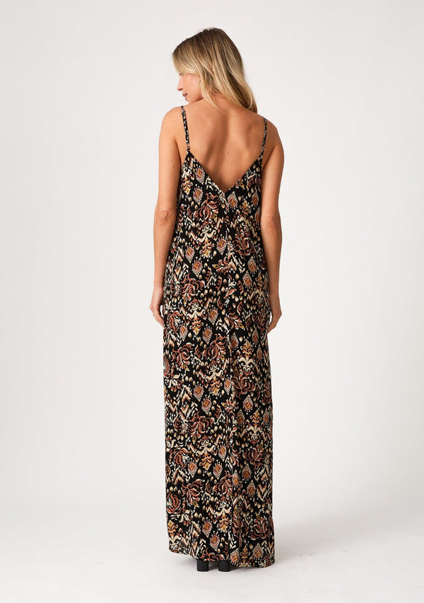 [Color: Black/Taupe] A back facing image of a blonde model wearing a best selling sleeveless maxi dress in a brown bohemian print. With adjustable spaghetti straps, a deep v neckline in the front and back, side pockets, and a flowy cocoon fit. 