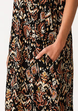 [Color: Black/Taupe] A close up side facing image of a blonde model wearing a best selling sleeveless maxi dress in a brown bohemian print. With adjustable spaghetti straps, a deep v neckline in the front and back, side pockets, and a flowy cocoon fit. 