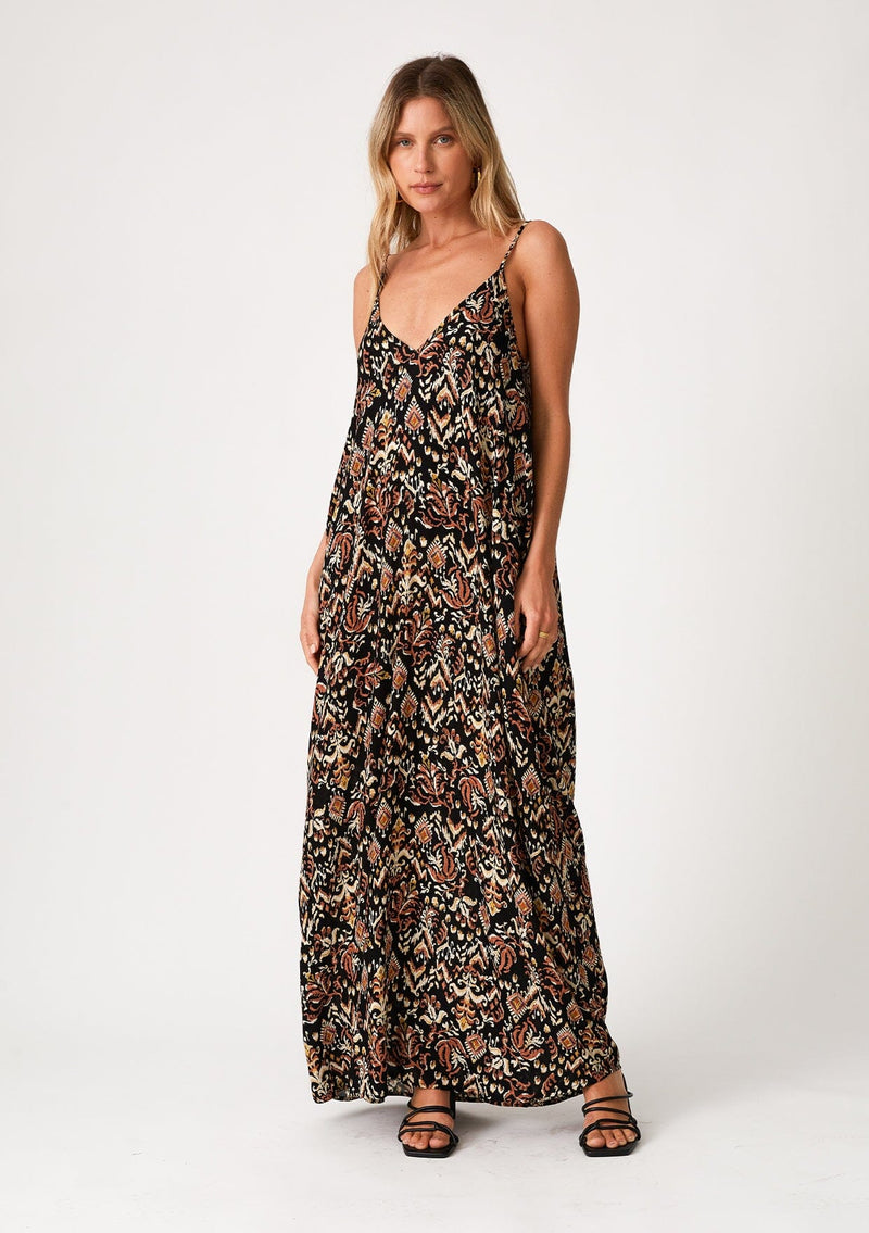 [Color: Black/Taupe] A front facing image of a blonde model wearing a best selling sleeveless maxi dress in a brown bohemian print. With adjustable spaghetti straps, a deep v neckline in the front and back, side pockets, and a flowy cocoon fit. 