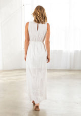 [Color: Ivory] A back facing image of a blonde model wearing a white maxi dress with all over lace trim, a split v neckline with tassel ties, and an elastic waistline. 