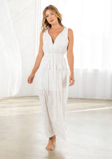 [Color: Ivory] A front facing image of a blonde model wearing a white maxi dress with all over lace trim, a split v neckline with tassel ties, and an elastic waistline. 