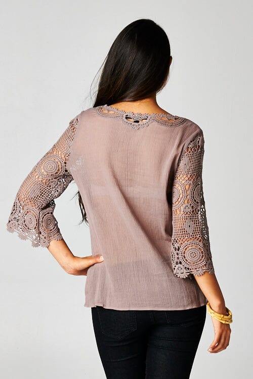 [Color: Dusty Orchid] A back facing image of a brunette model wearing a 3-4 sleeve cotton blouse with delicate crochet lace details. 