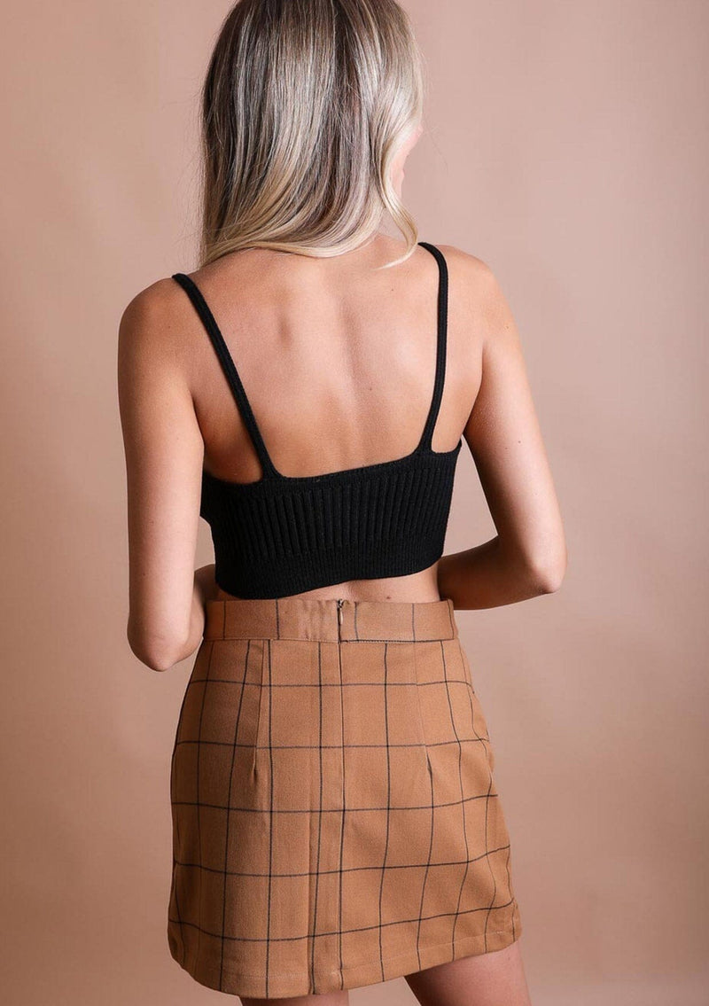 [Color: Black] A blonde model wearing a rib knit crop top in black. Featuring a v neckline, spaghetti straps, and a body hugging silhouette. A soft and cozy top crafted in stretchy fabric, perfect for layering or wearing on its own. 