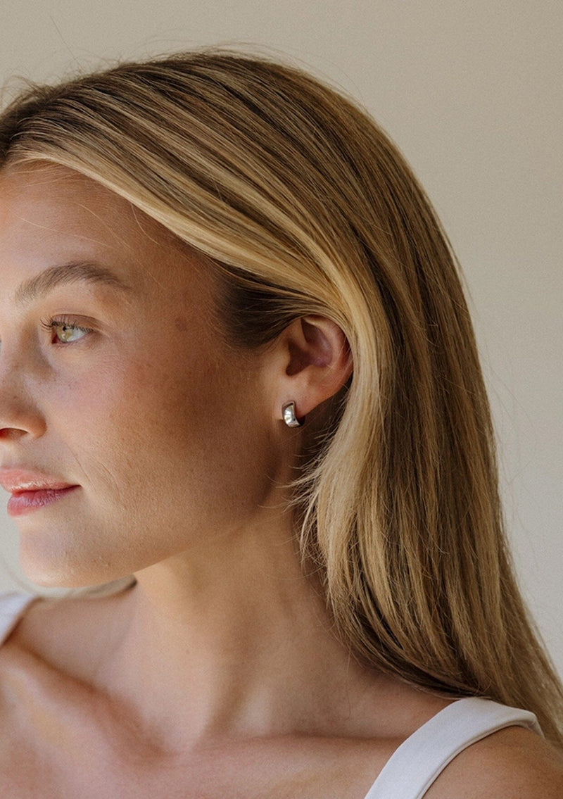 Woman wearing a silver huggie earring with a neutral background