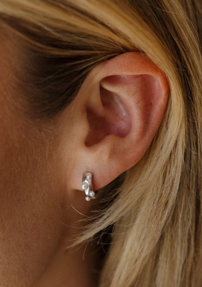 Close-up of an ear wearing a silver earring with pearls.